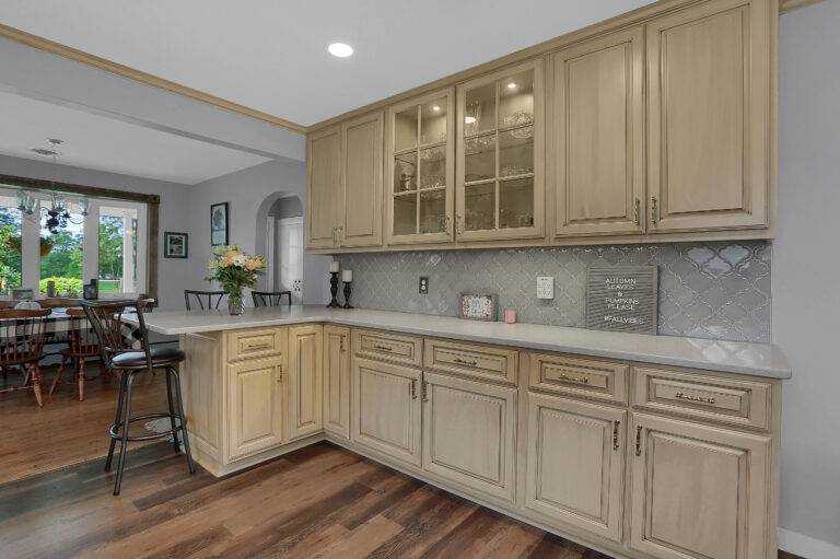A spacious kitchen with beige cabinets, glass cupboard doors, and a grey tiled backsplash